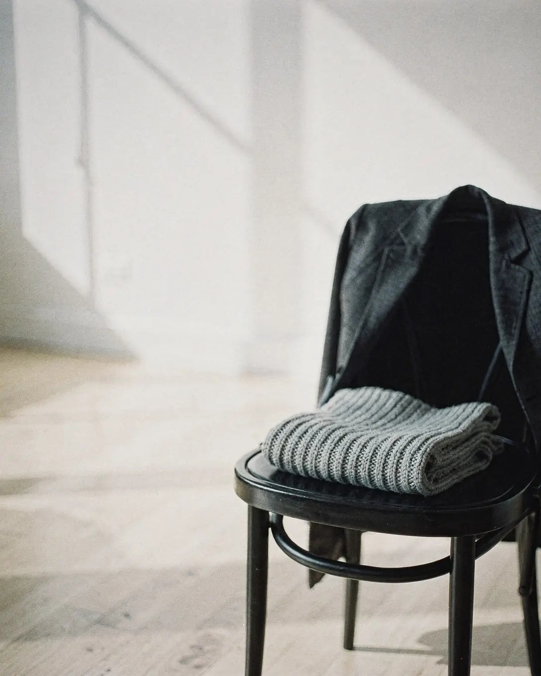 A charcoal jacket and a grey knit scarf on a black bentwood chair in a sunlit loft