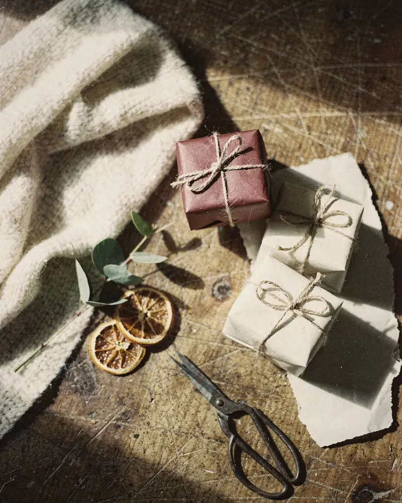 Three small gifts wrapped in bordeaux and ivory paper with twine, eucalyptus and dried orange slices on a wooden floor